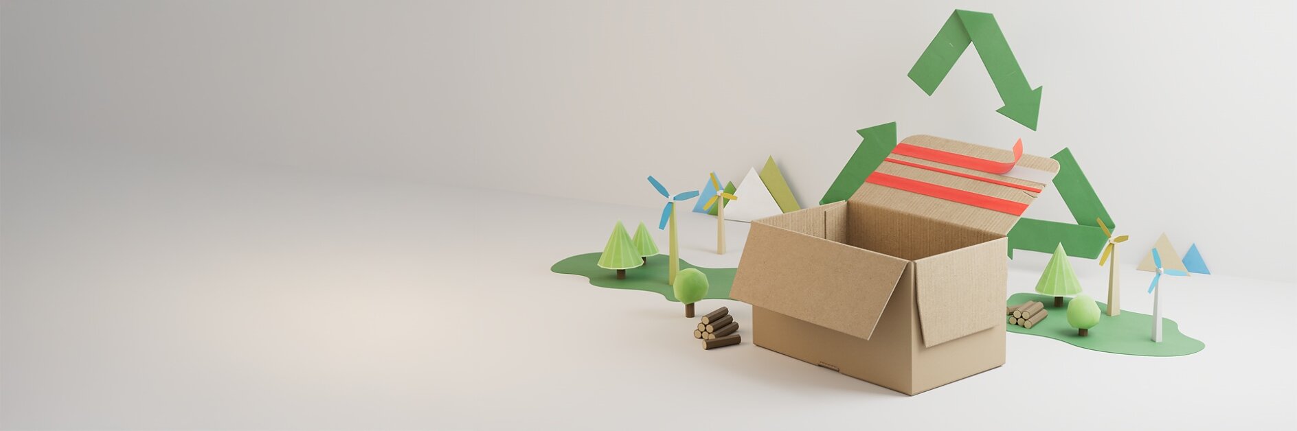 A cardboard box sits open on a white surface, sealed with tesa tape, with small models of trees, wind turbines, and logs behind it. A green recycling symbol is displayed on the wall in the background.